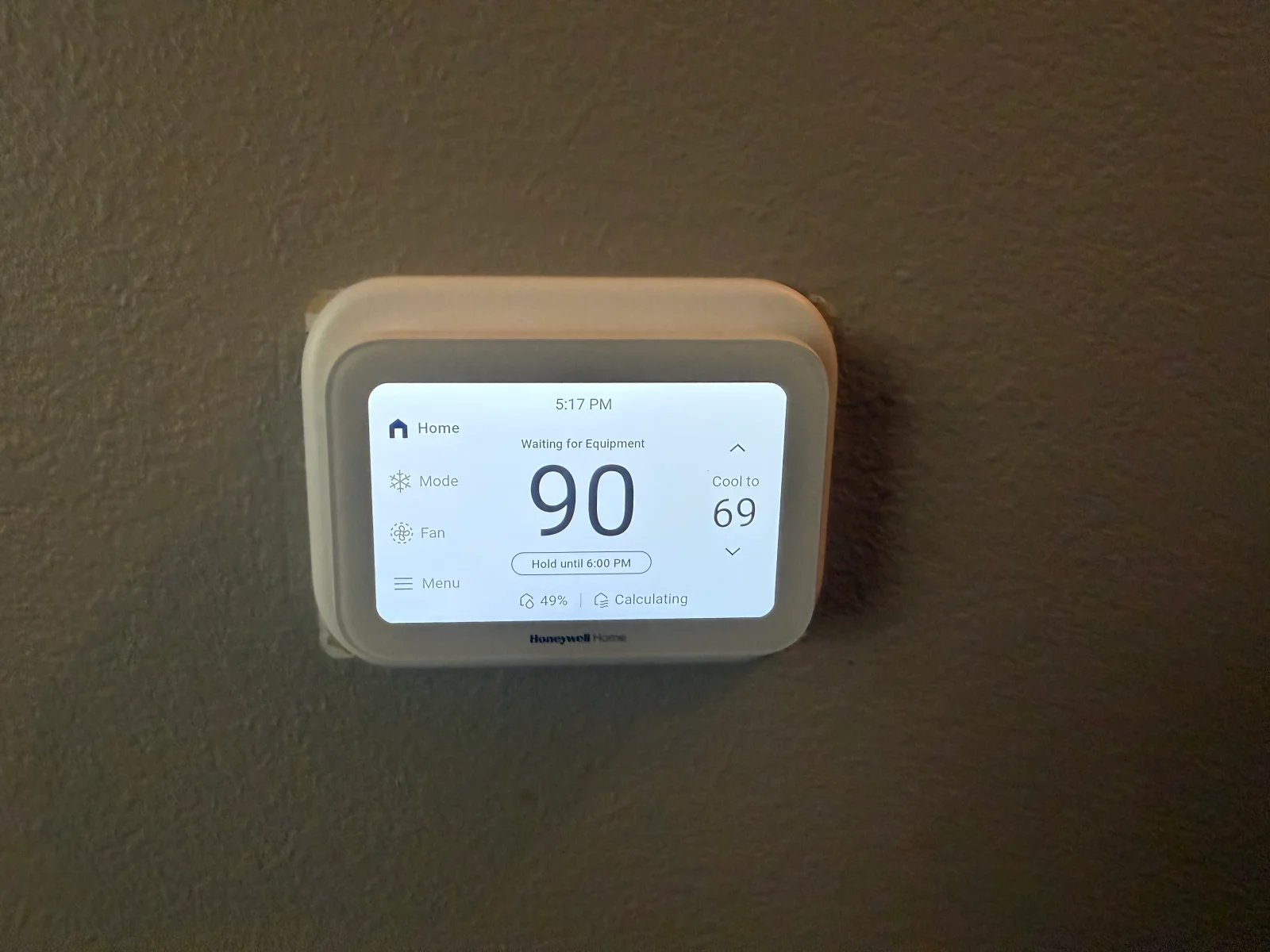 Honeywell Home touchscreen smart thermostat mounted on textured wall, showing cool setpoint and humidity display